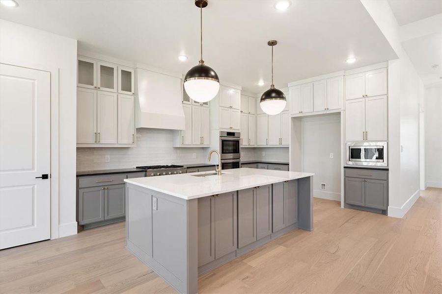 Kitchen featuring gray cabinets, stainless steel appliances, custom exhaust hood, and light hardwood / wood-style floors