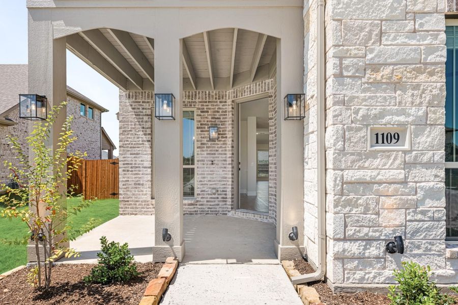 Home entrance with arched brick doorway, stone exterior, wall sconces, and house number 1109 Home entrance with arched brick doorway, stone exterior, wall sconces, and house number 1109