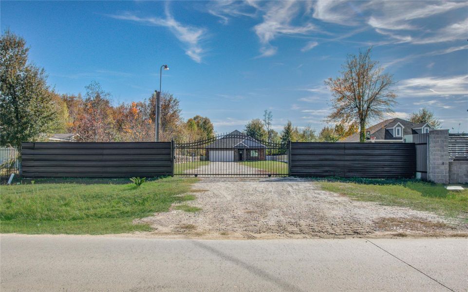 A gated property with a spacious driveway leading to a house, surrounded by trees and a clear sky, offering privacy and a serene setting.