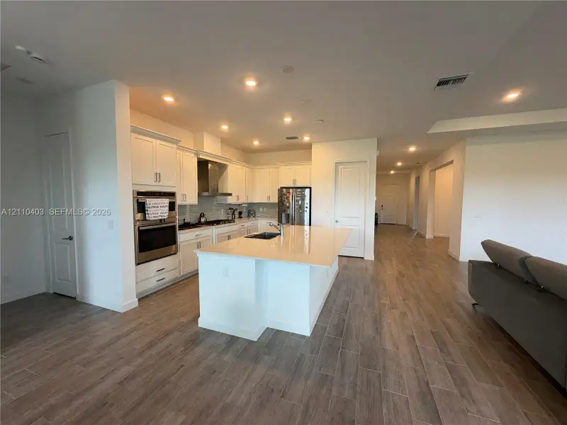 Kitchen featuring white cabinetry, an expansive center island with stone-surface countertop, stainless steel double wall oven, and wood-finish flooring