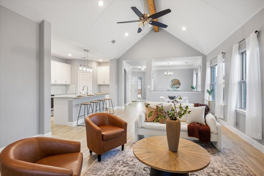 Living room featuring light wood-type flooring, ceiling fan with notable chandelier, vaulted ceiling with beams, and sink