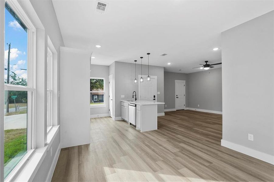 Kitchen featuring stainless steel dishwasher, decorative light fixtures, light hardwood / wood-style flooring, white cabinetry, and a center island