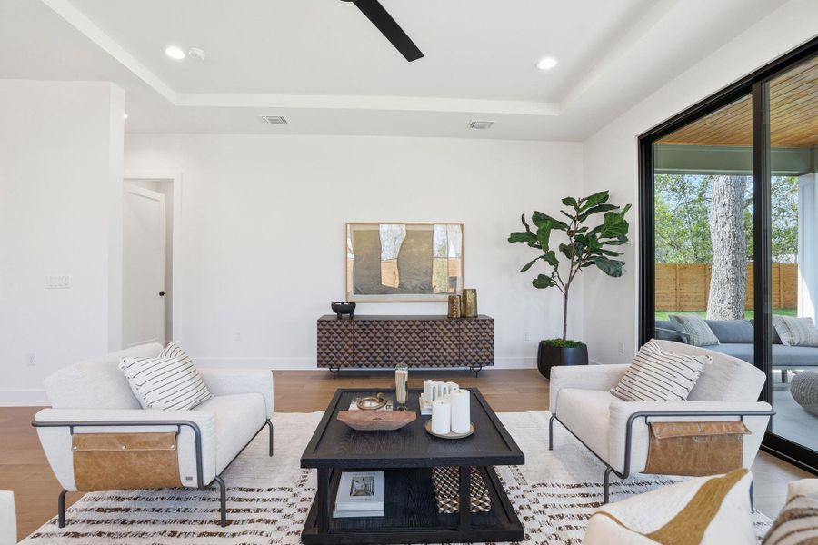 Living area with a raised ceiling, wood finished floors, ceiling fan, and recessed lighting