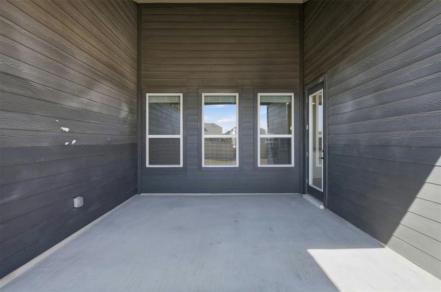 Covered patio with durable concrete flooring, dark horizontal siding, three large windows, and a glass-paneled exterior door