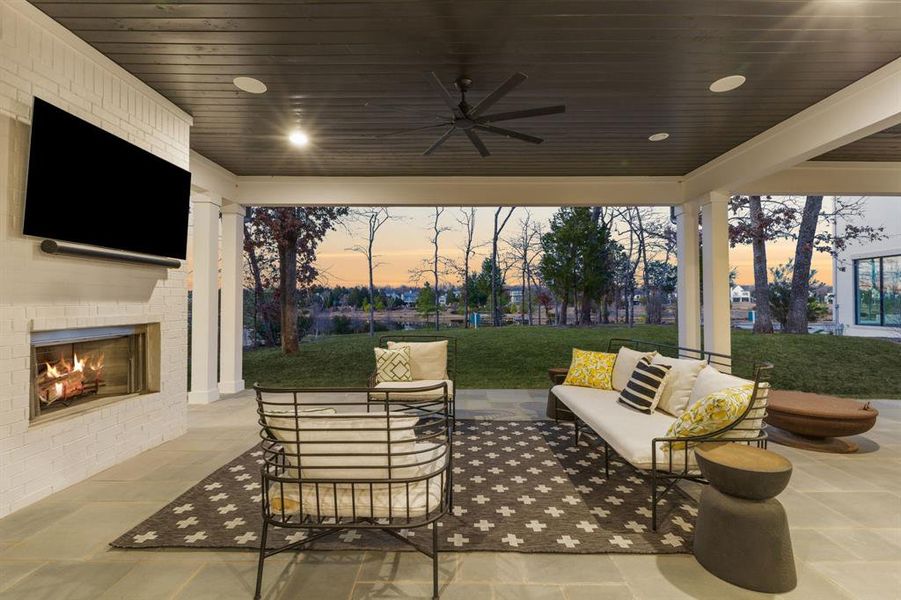 Patio terrace at dusk with an outdoor living space with a fireplace, a lawn, and a ceiling fan Patio terrace at dusk with an outdoor living space with a fireplace, a lawn, and a ceiling fan
