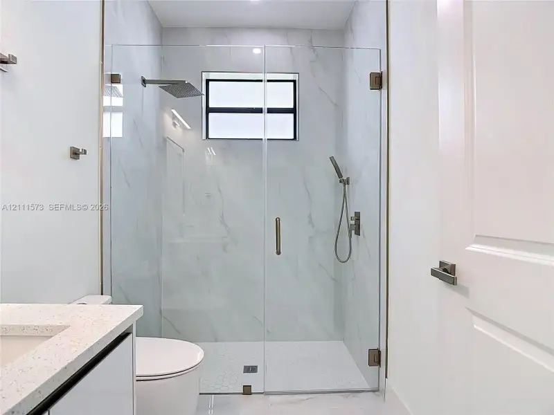 Walk-in shower featuring a frameless glass enclosure, rain-style shower head, handheld sprayer, and large-format wall tile with hexagonal floor tile