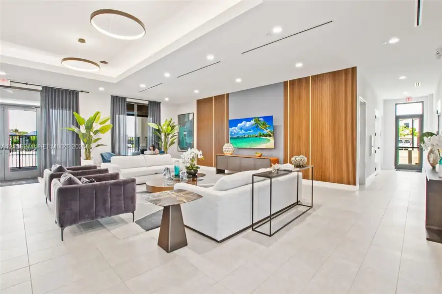Open-concept space featuring large-format tile flooring, a tray ceiling with recessed lighting, prominent vertical wood-finish wall paneling, and dual circular pendant fixtures