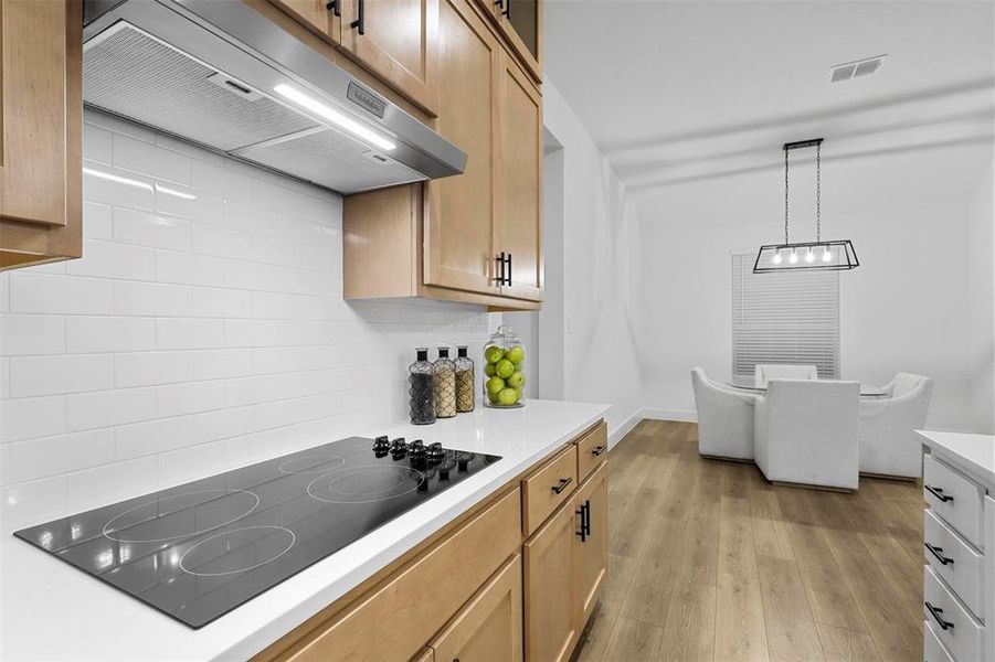 Kitchen with range hood, decorative light fixtures, decorative backsplash, light hardwood / wood-style floors, and black electric cooktop