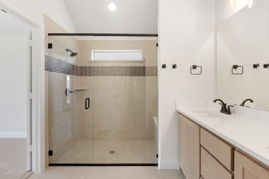 Bathroom with glass-enclosed tile shower, wood vanity, and white quartz countertop with dark fixtures