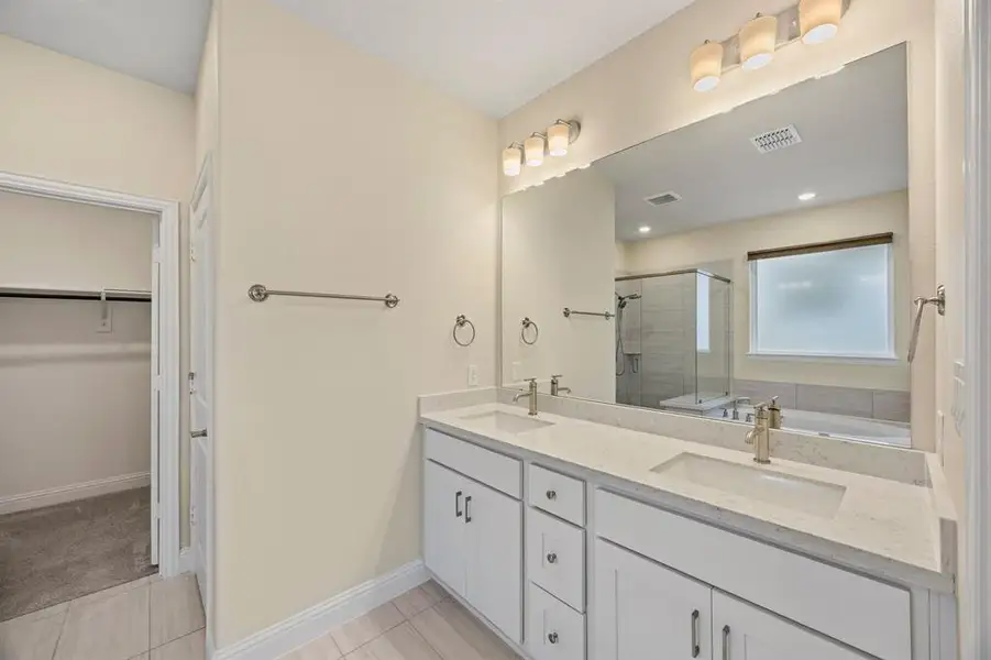 Full bathroom with double vanity, a garden tub, a shower stall, a spacious closet, and light tile patterned floors
