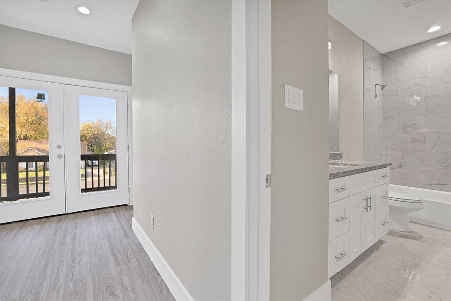 Full bathroom with french doors, tiled shower / bath combo, wood-type flooring, toilet, and vanity