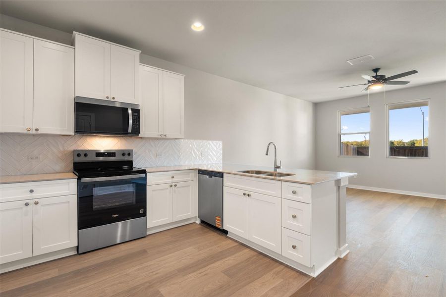 Kitchen featuring appliances with stainless steel finishes, backsplash, white cabinets, a peninsula, and recessed lighting