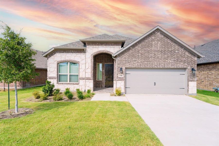 French provincial home featuring brick siding, stone siding, concrete driveway, a lawn, and a garage