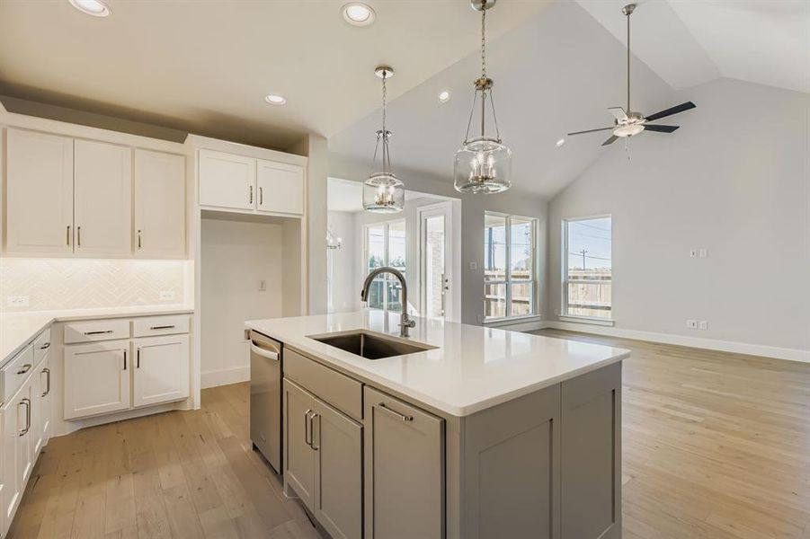 Kitchen featuring decorative backsplash, light wood-type flooring, decorative light fixtures, a chandelier, and a center island with sink