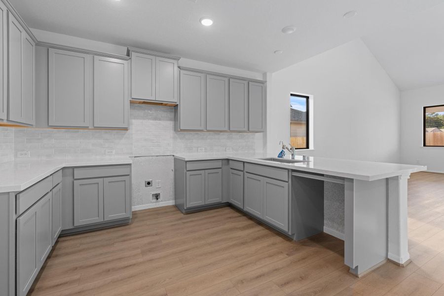 This light and bright kitchen features a large quartz island, white cabinets, a large sink overlooking your family room, recessed lighting, and beautiful backsplash.