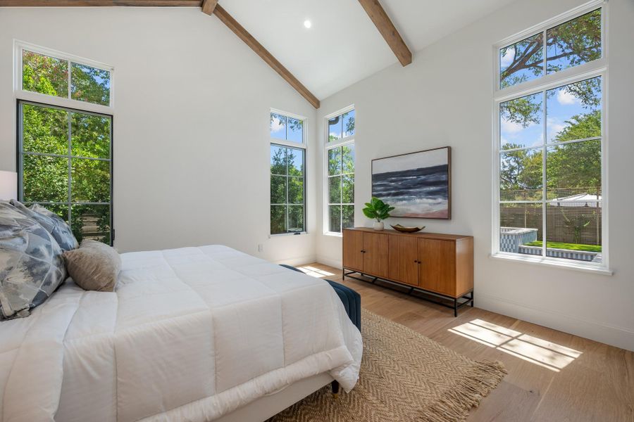 Beamed vaulted ceilings and tall windows frame peaceful views in this hardwood-floored bedroom.