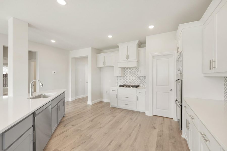 Open kitchen with white and gray cabinets, patterned tile backsplash, and light wood floors