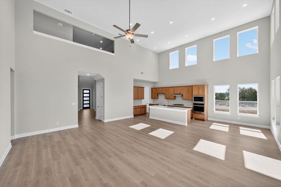 Unfurnished living room featuring light wood finished floors, a high ceiling, a ceiling fan, and recessed lighting Unfurnished living room featuring light wood finished floors, a high ceiling, a ceiling fan, and recessed lighting