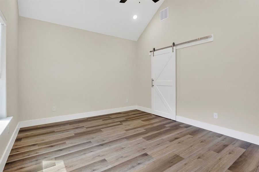 Master bedroom with white sliding barn door for ensuite bathroom and high base boards for easy cleaning and wood looking vinyl luxury flooring, and cathedral ceilings.