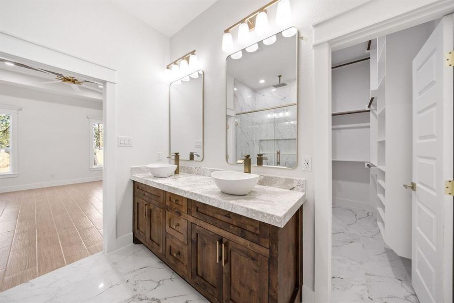 Full bathroom with double vanity, light marble finish floors, a marble finish shower, a walk in closet, and a ceiling fan