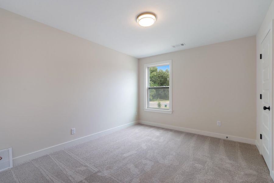 Wall-to-wall carpeting, single window with white trim, white paneled door with black hardware, and a ceiling-mounted light fixture Wall-to-wall carpeting, single window with white trim, white paneled door with black hardware, and a ceiling-mounted light fixture