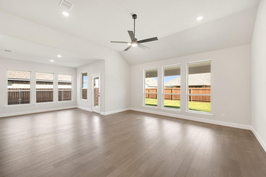 Open living room with vaulted ceiling, ceiling fan, hardwood floors, and large windows overlooking backyard