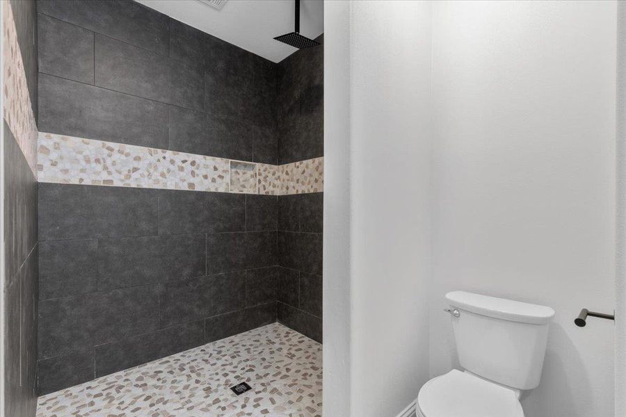 Dark tile walls and a stone mosaic floor define this modern walk-in shower space. Dark tile walls and a stone mosaic floor define this modern walk-in shower space.