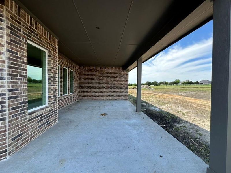 Expansive covered patio featuring a concrete surface, brick exterior wall, multiple windows, and a dark soffit