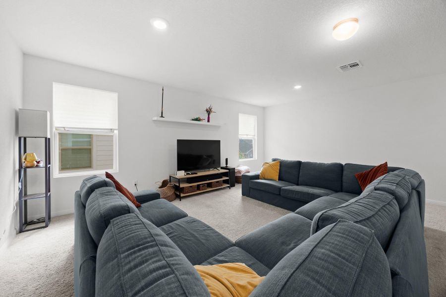 Carpeted living space featuring recessed lighting, a ceiling-mounted light fixture, white walls, and multiple windows with roller shades