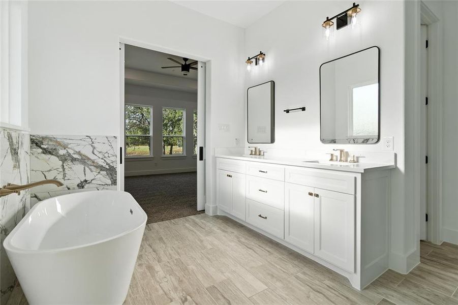 Full bath with double vanity, a freestanding tub, wood finished floors, and ceiling fan