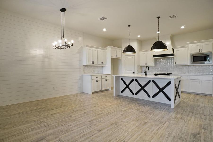 Kitchen featuring light hardwood / wood-style floors, a center island with sink, hanging light fixtures, stainless steel microwave, and premium range hood