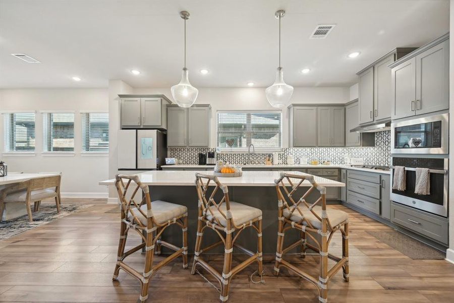 Kitchen featuring backsplash, decorative light fixtures, hardwood / wood-style flooring, gray cabinets, and a kitchen island