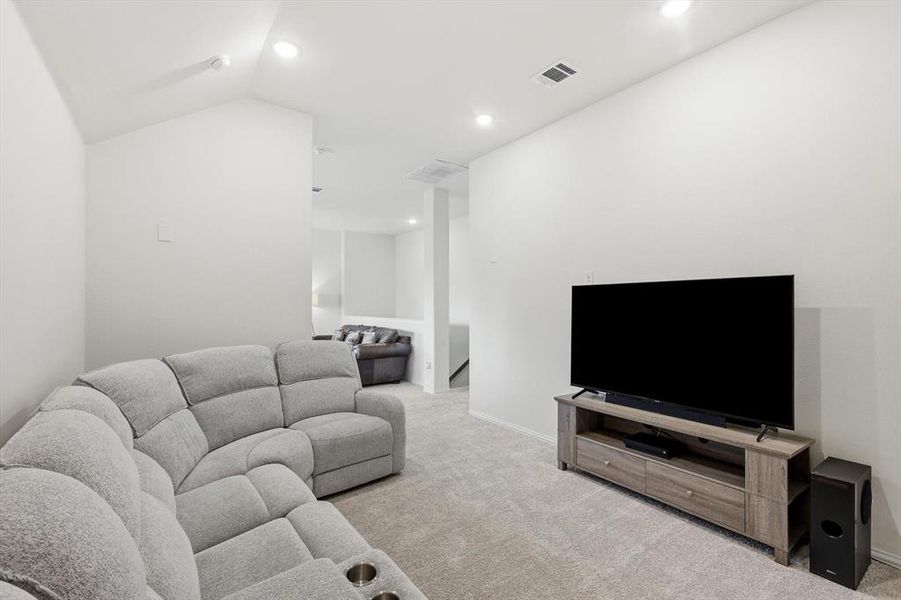 Carpeted entertainment area featuring white walls, recessed lighting, and a light wood-finish media console