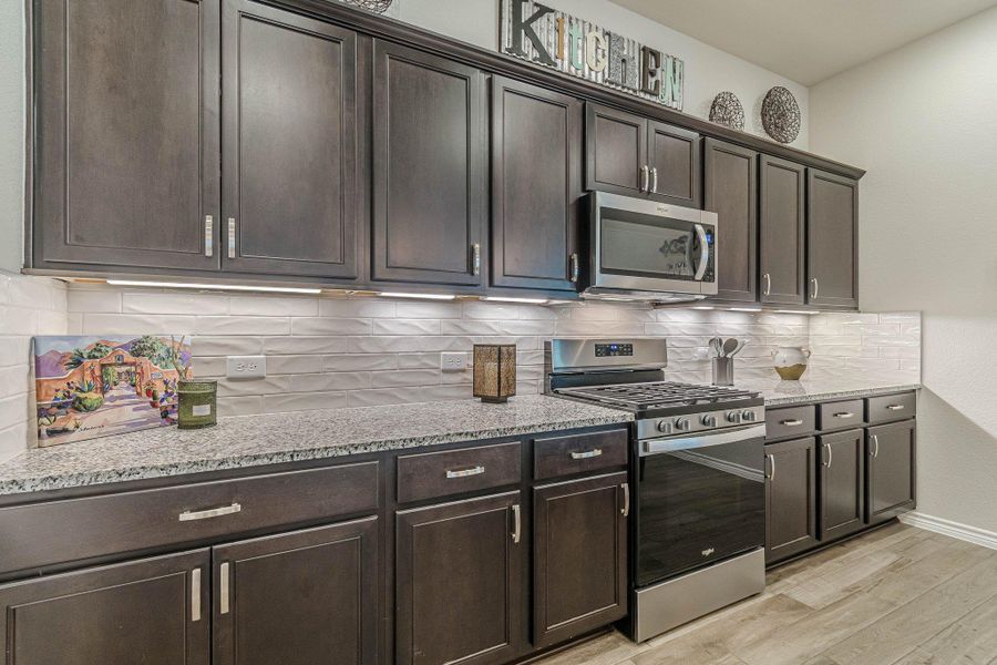 Kitchen featuring appliances with stainless steel finishes, light wood-style flooring, dark brown cabinets, light stone counters, and backsplash