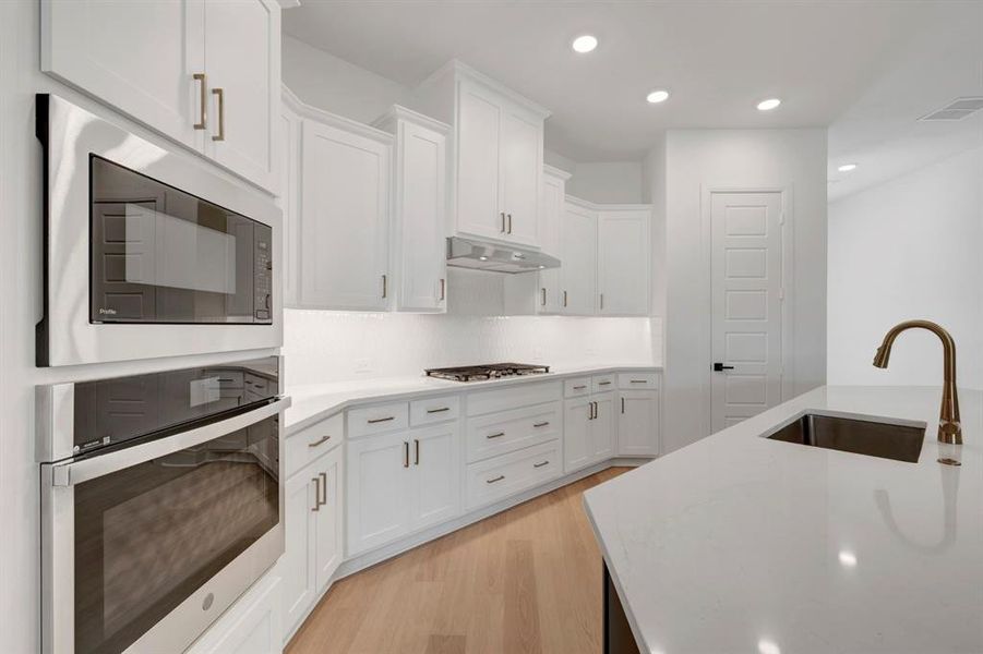Kitchen with stainless steel appliances, white cabinets, light wood finished floors, recessed lighting, and light stone countertops