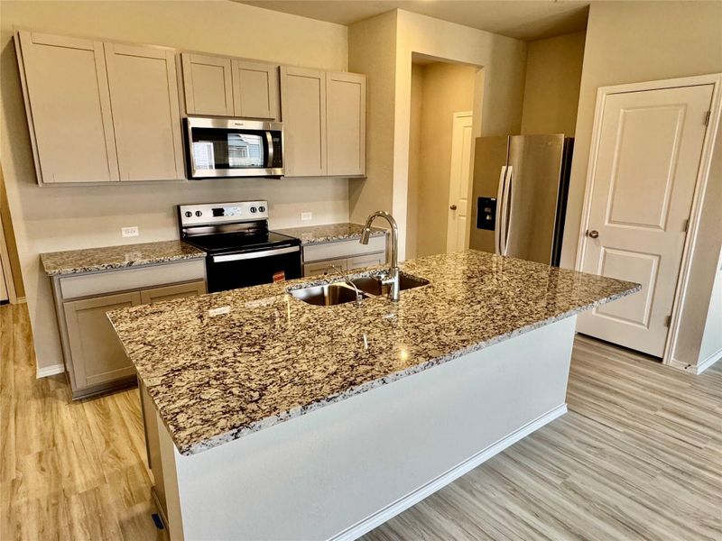 Kitchen with stainless steel appliances, light stone counters, light wood-style flooring, and a kitchen island with sink
