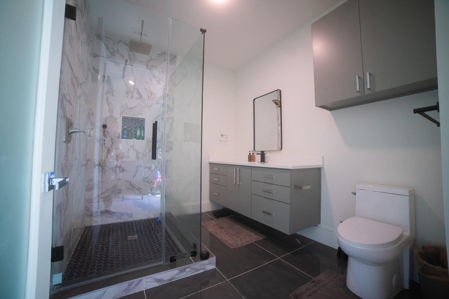 The private ensuite is a study in modern design, featuring a spacious walk-in shower enclosed by seamless glass doors. This transparent design maintains an open, airy feel, allowing the room’s natural light to highlight the premium tile work and high-end fixtures