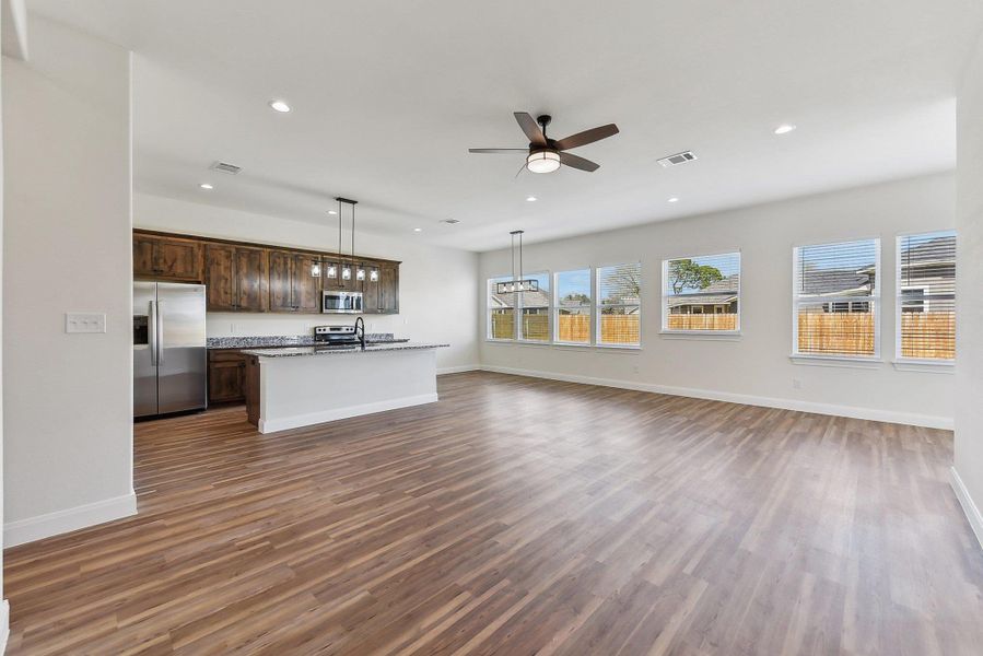 Kitchen featuring visible vents, open floor plan, a center island with sink, wood finished floors, and stainless steel appliances Kitchen featuring visible vents, open floor plan, a center island with sink, wood finished floors, and stainless steel appliances