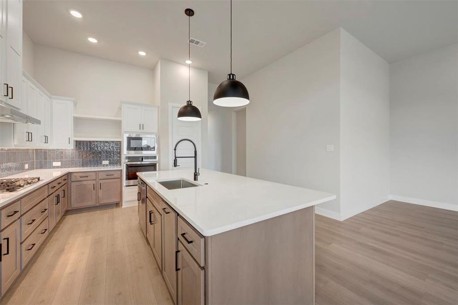 Dual tone kitchen featuring two tone cabinets, open shelves, light wood-type flooring, decorative backsplash, and stainless steel appliances