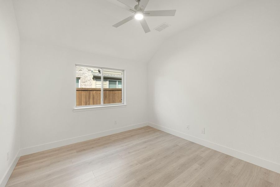 Empty bedroom with vaulted ceiling, ceiling fan, light wood floors, and single window