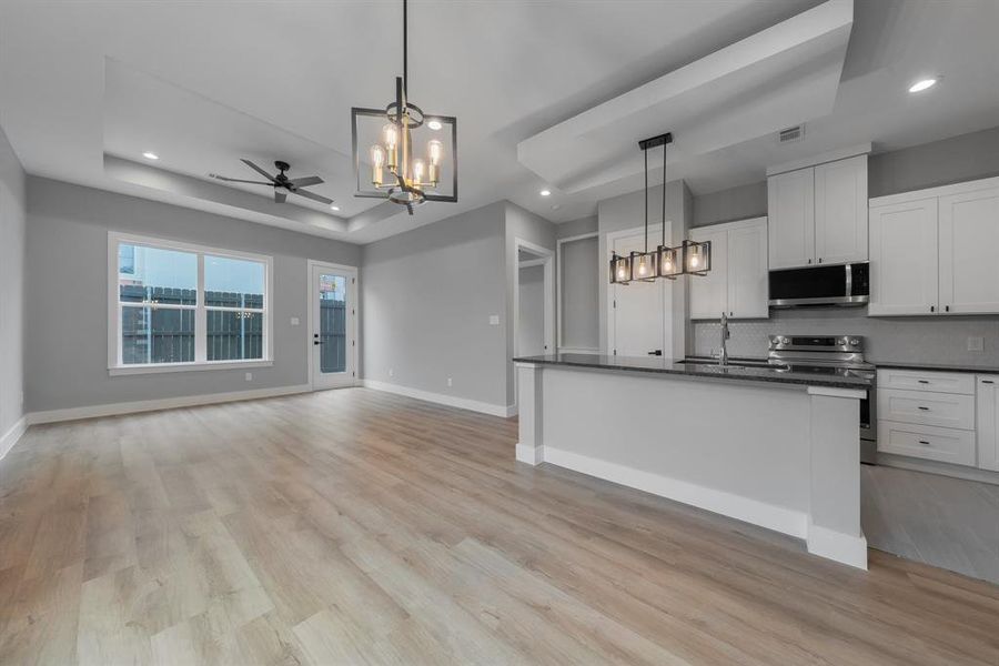 Kitchen with dark countertops, a sink, appliances with stainless steel finishes, a raised ceiling, and ceiling fan with notable chandelier