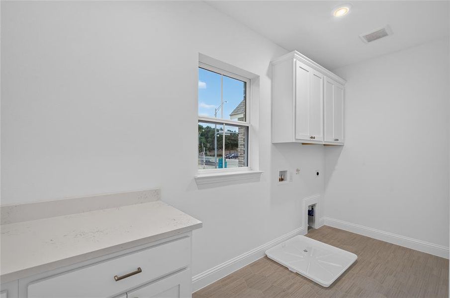 Utility room featuring white shaker-style cabinetry, a window with natural light, a countertop with storage below, and wood-finish flooring Utility room featuring white shaker-style cabinetry, a window with natural light, a countertop with storage below, and wood-finish flooring