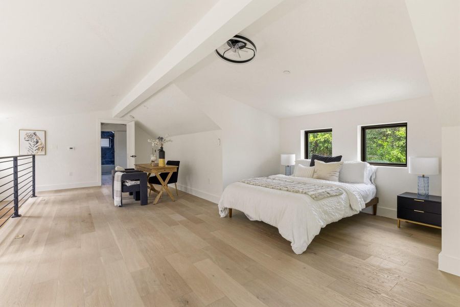 Bright, open-concept room featuring light wood-finish flooring, white walls, and a sloped ceiling with a modern ceiling fan