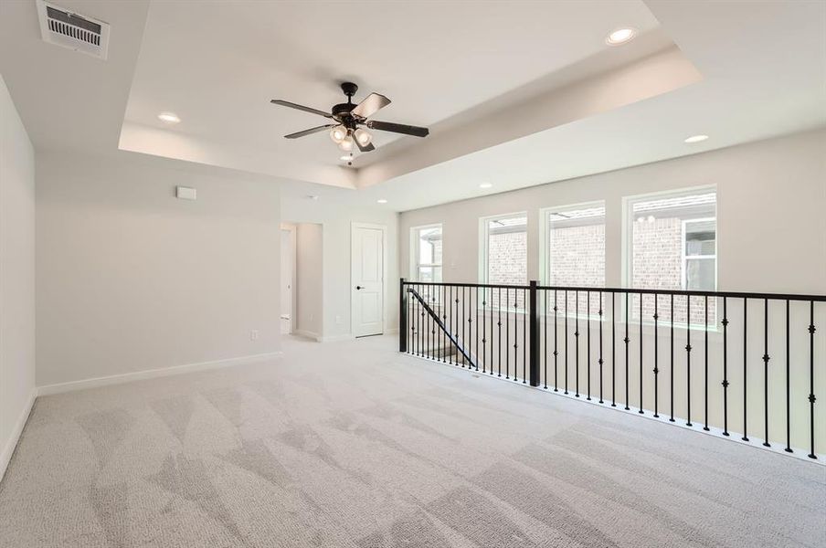 Carpeted empty room with ceiling fan and a raised ceiling