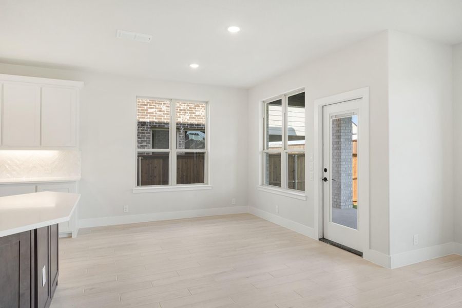 Bright dining area with light wood floors, white walls, two windows, and a glass back door