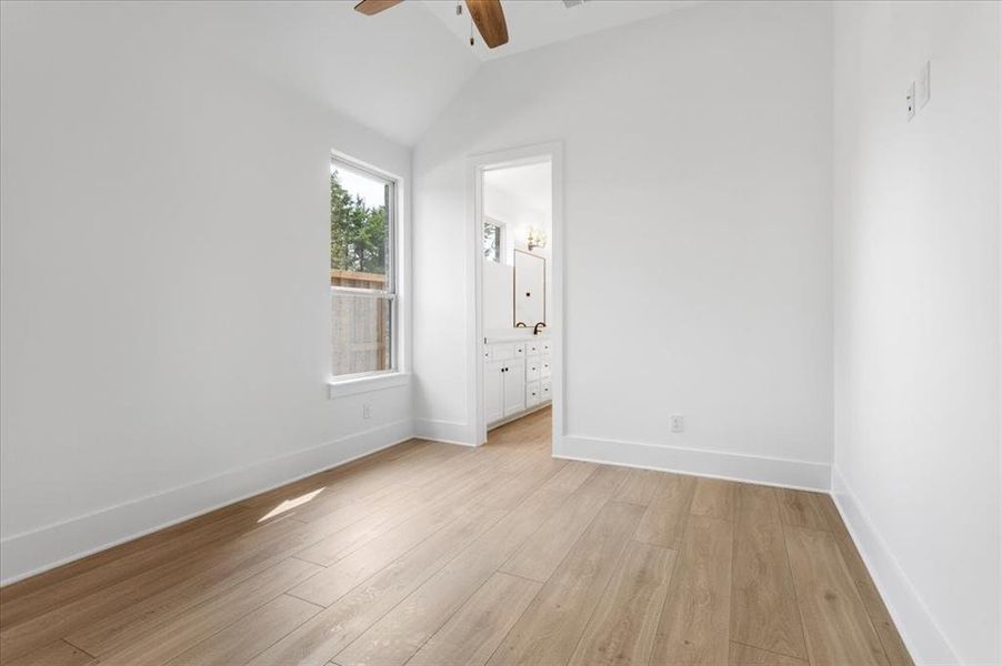 Unfurnished bedroom featuring light wood-style flooring, lofted ceiling, connected bathroom, and a ceiling fan