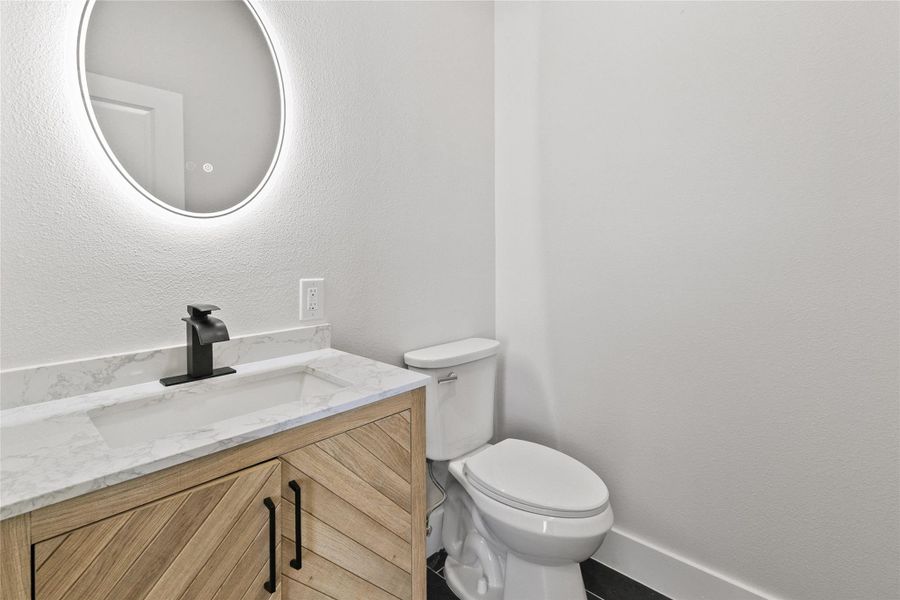 Half bath conveniently located near the entryway and home office, featuring modern finishes and an illuminated mirror.