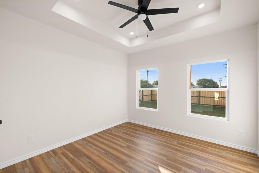 Empty room featuring a raised ceiling, wood finished floors, recessed lighting, and ceiling fan Empty room featuring a raised ceiling, wood finished floors, recessed lighting, and ceiling fan