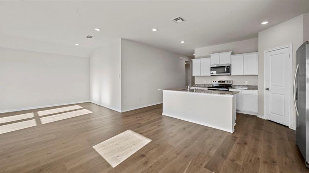 Kitchen with white cabinetry, stainless steel appliances, an island with sink, dark wood-type flooring, and recessed lighting
