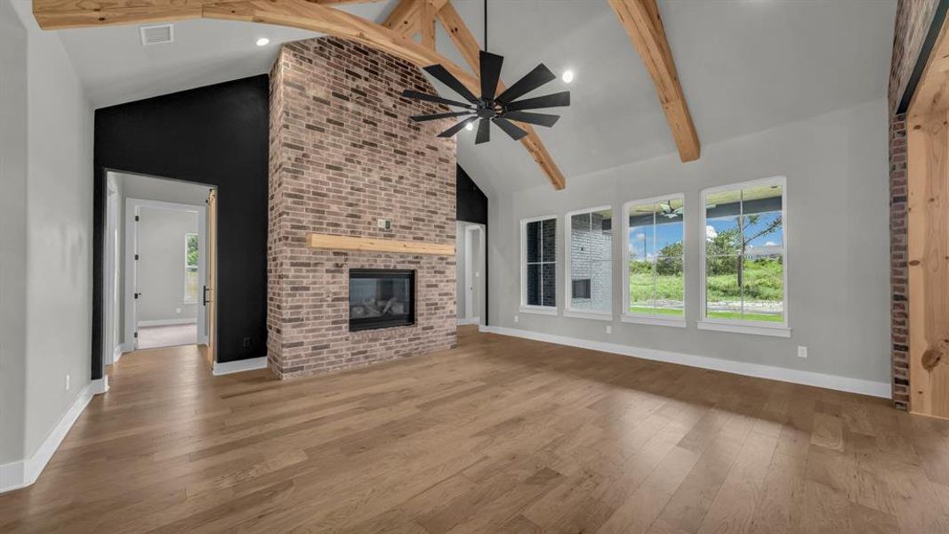 Vaulted ceilings with exposed wood beams, a brick fireplace with a wood mantel, and multiple windows